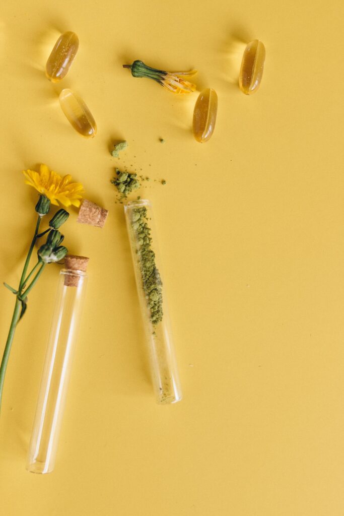 Capsules, flowers and herbs in vials scattered around a yellow table