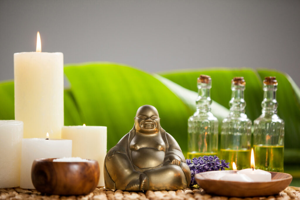 laughing buddha figurine lit candle massage oil bottles sea salt
