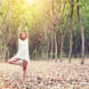yoga pose done by young asian woman in white costume on green grass in the green forest