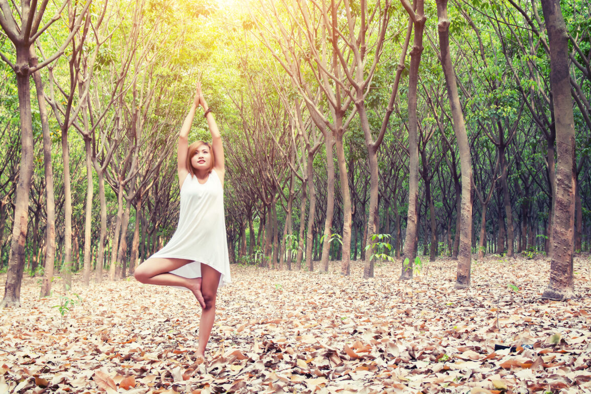yoga pose done by young asian woman in white costume on green grass in the green forest