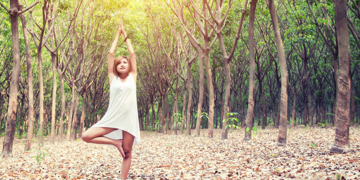 yoga pose done by young asian woman in white costume on green grass in the green forest