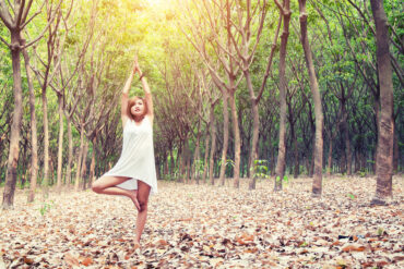 yoga pose done by young asian woman in white costume on green grass in the green forest