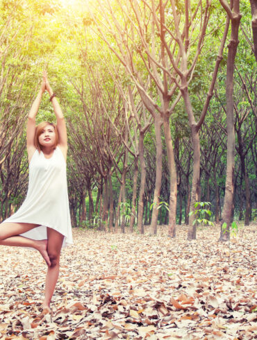 yoga pose done by young asian woman in white costume on green grass in the green forest
