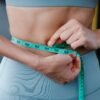 a woman measuring her waist with an inch tape