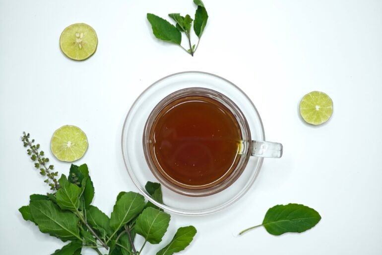 herbal tea in a cup and lime and herbs scattered around it