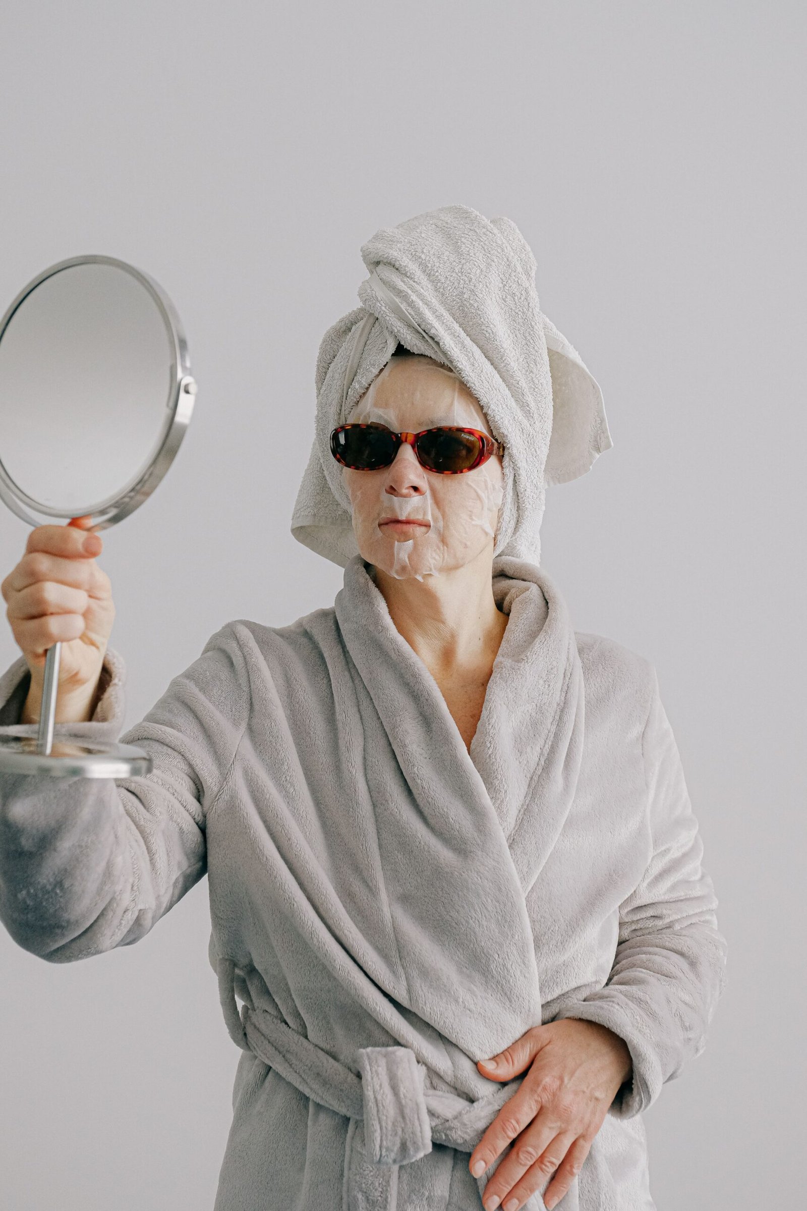 a woman with a face mask on holding a mirror for Ayurvedic Anti-Aging Secrets