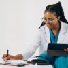 a doctor writing something down on her notebook while holding a device
