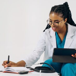 a doctor writing something down on her notebook while holding a device