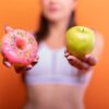a woman holding a donut and a green apple