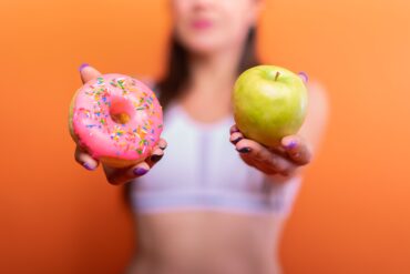 a woman holding a donut and a green apple
