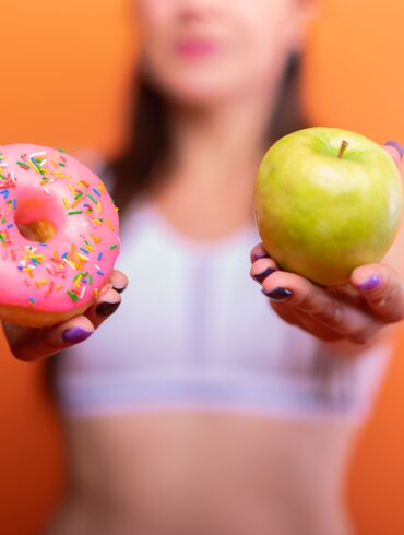 a woman holding a donut and a green apple