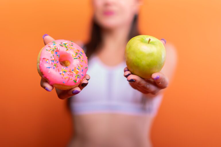 a woman holding a donut and a green apple
