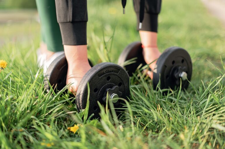 a girl picking up dumbbells in a park for Gym Exercises